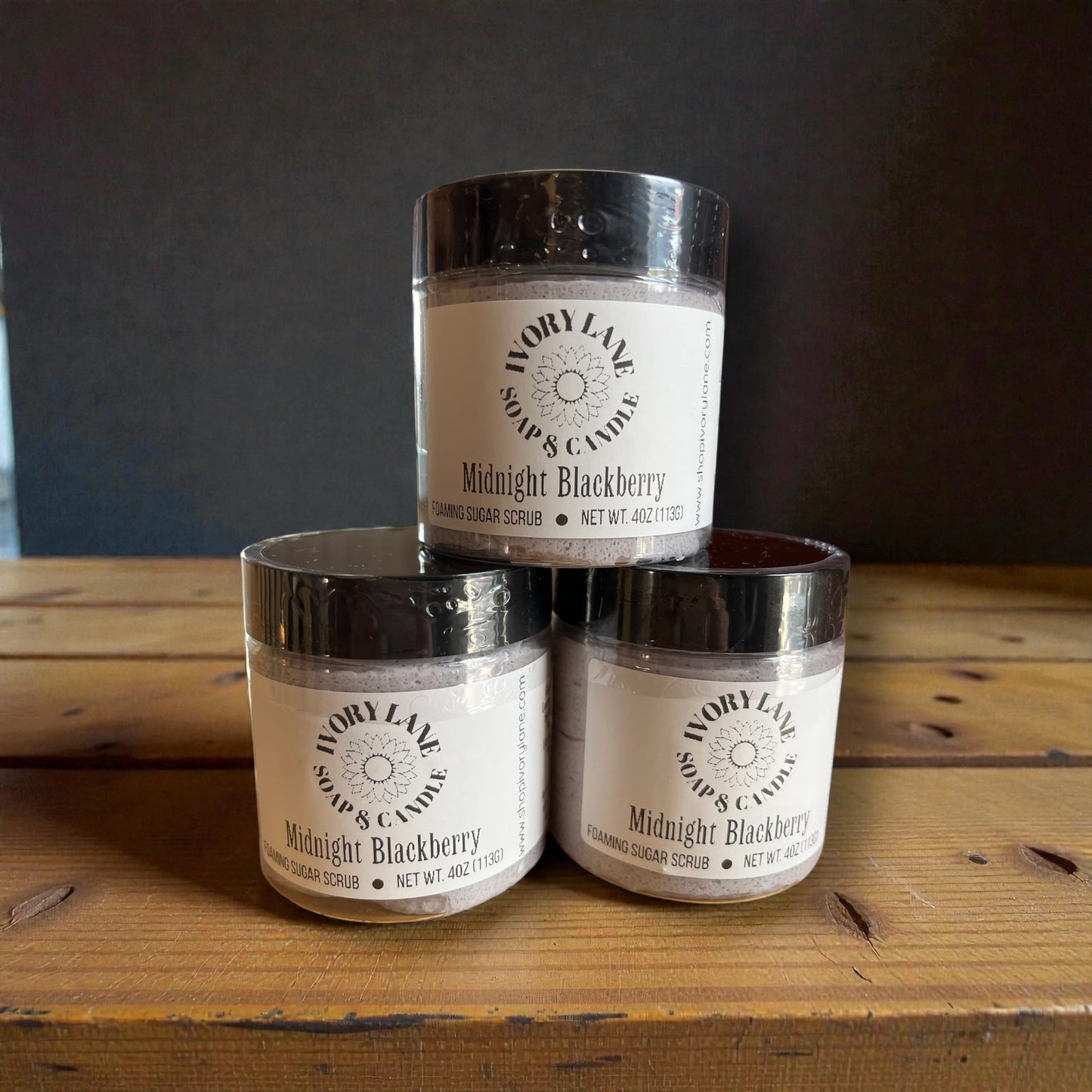 Three jars of 'Midnight Blackberry' scrub from Ivory Lake Soap & Candle on a wooden surface with a dark background.