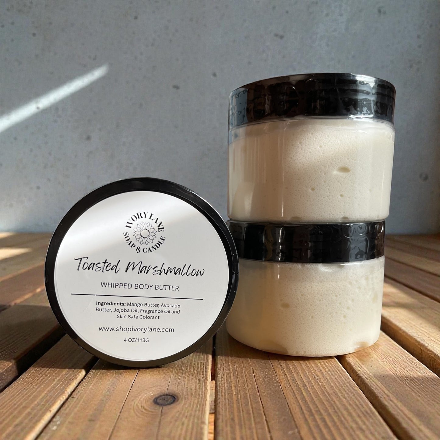 Two containers of 'Toasted Marshmallow' whipped body butter on a wooden surface with a gray background.