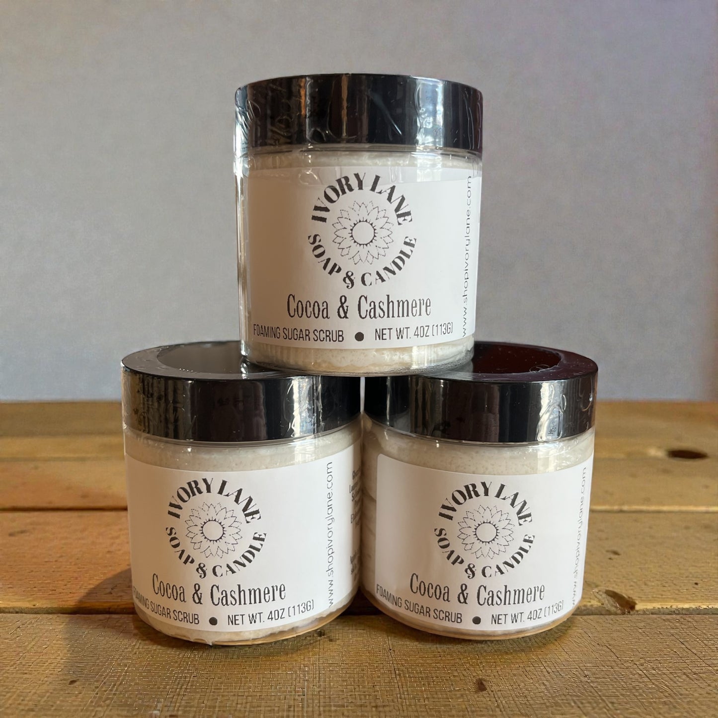 Three jars of Ivory Lane Soap & Candle Cocoa & Cashmere scrub stacked on a wooden surface.