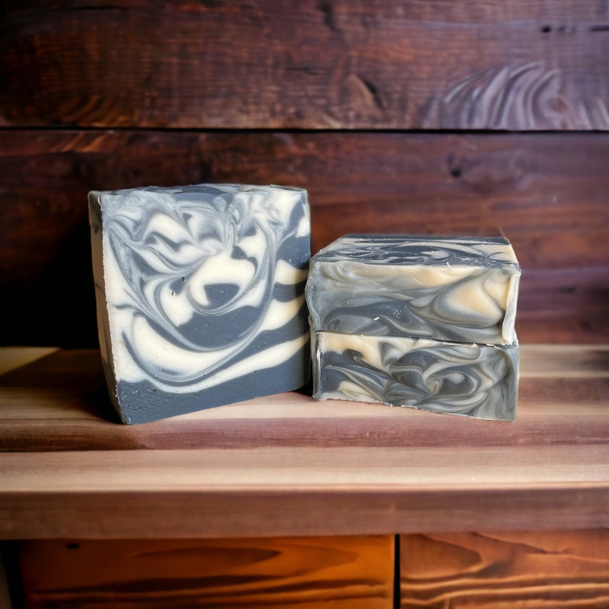 Two bars of marbled cold process soap with a swirl pattern, placed on a wooden surface.