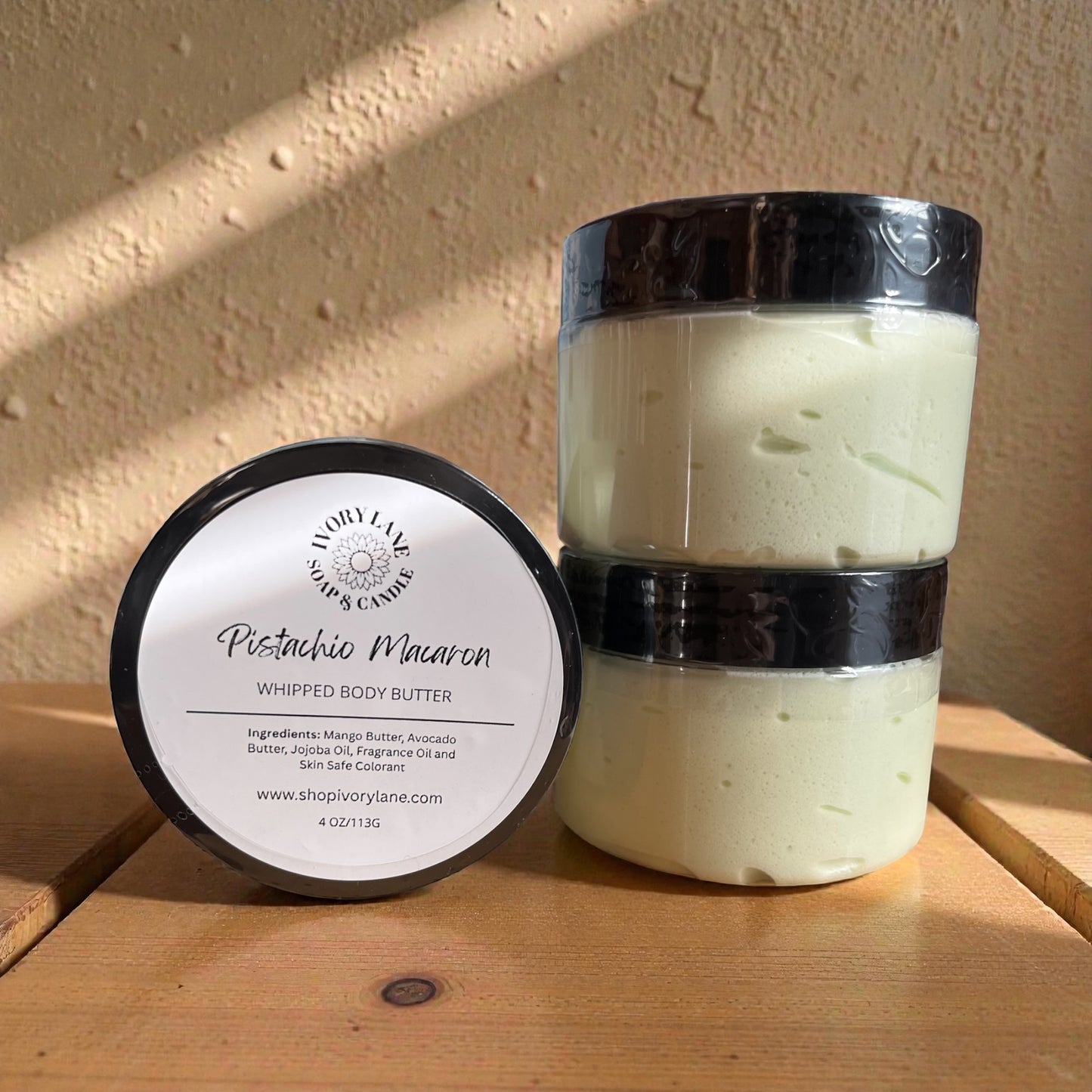 Pistachio Macaron whipped body butter jar and container on a wooden surface with a beige wall background.